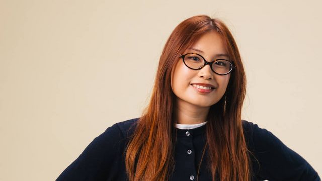 Junge Werkstudentin mit Brille vor Studiohintergrund.