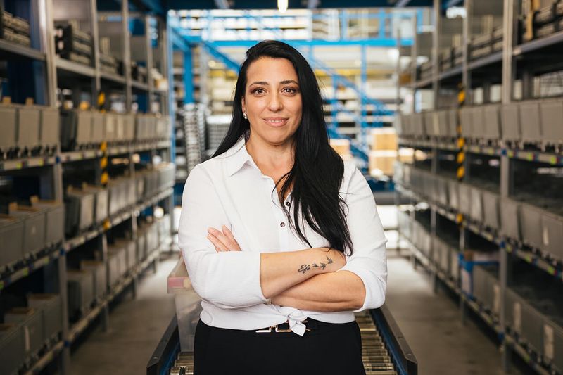 Apollo-Mitarbeiterin mit verschränkten Armen im Logistiklager.