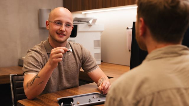 Ein Hörakustiker bei Apollo zeigt einem Kunden im Beratungsgespräch ein kleines Hörgerät.
