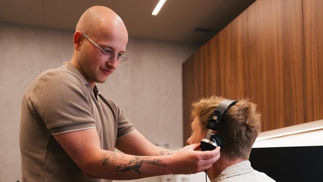 örakustiker setzt einem Kunden Kopfhörer für einen Hörtest auf.