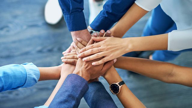 Aufeinandergelegte Hände als Symbol für Teamgeist.